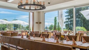 Ein modernes Restaurant mit hohen Decken, großen Fenstern und einer zentralen Kronleuchter.