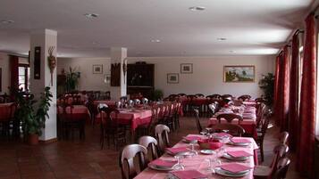 A dining area with multiple tables set for meals, chairs, and potted plants.