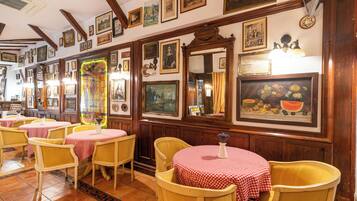 A restaurant interior with wooden beams, red and white checkered tablecloths, and various framed artworks on the walls.