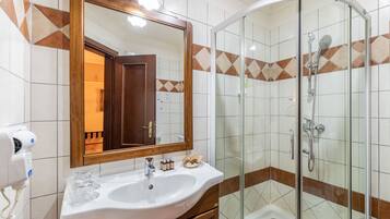 Un baño con un lavamanos blanco, un espejo grande y una ducha con cerramiento de vidrio.