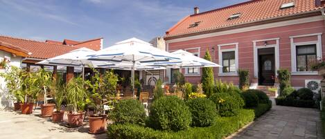 A courtyard with potted plants, outdoor seating, and a building with a red-tiled roof.