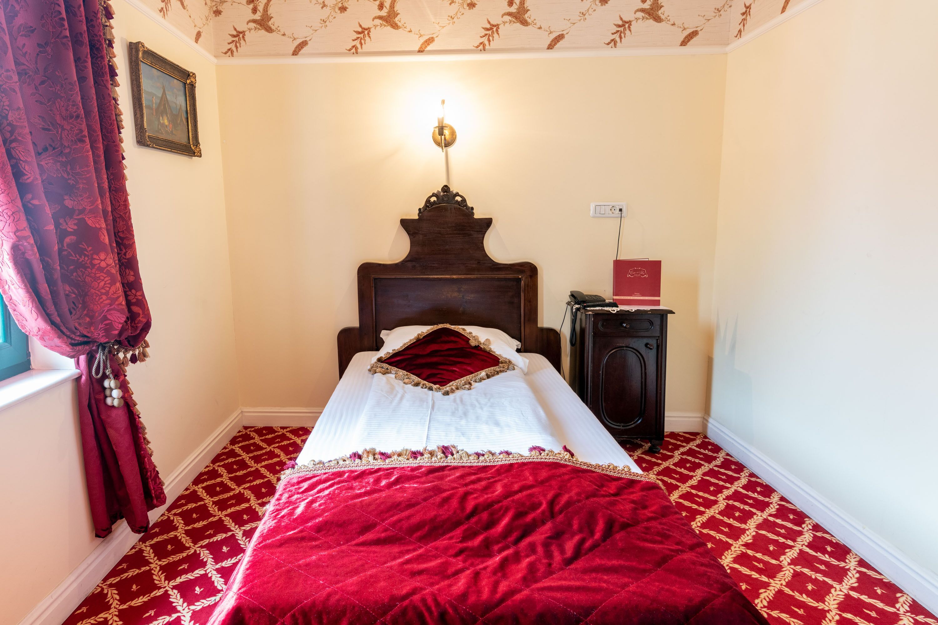 Una habitación con cama, mesita de noche, lámpara y alfombra estampada.