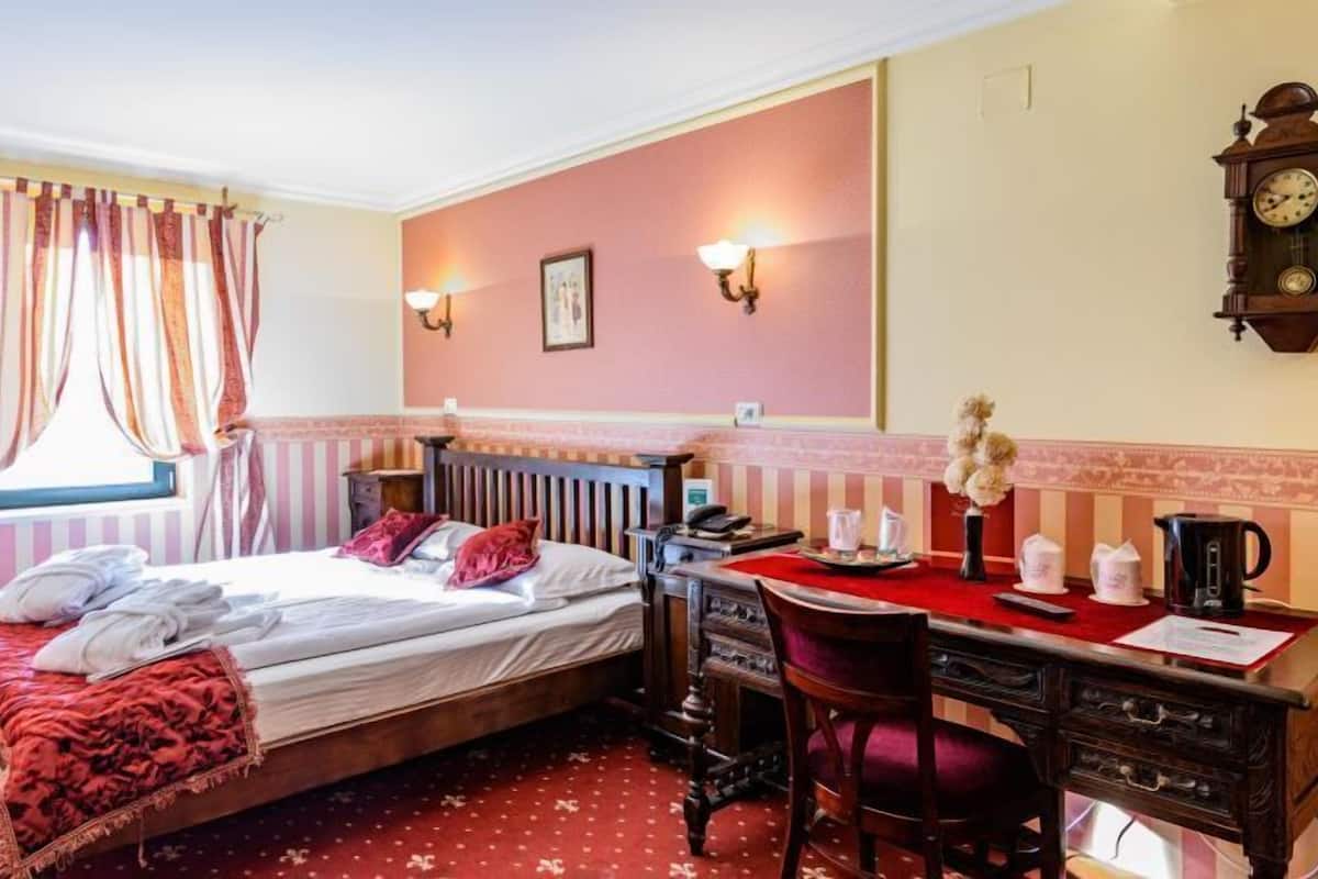 Una habitación de hotel con cama, escritorio, silla, reloj y ventana con cortinas.