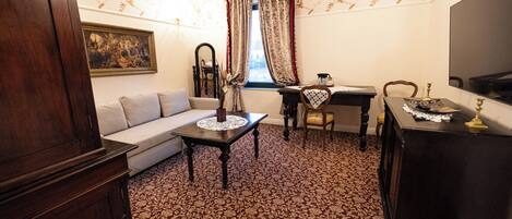 Una habitación con un sofá, una mesa con mantel de encaje, un escritorio, una silla y un armario.