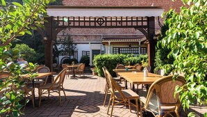 An outdoor patio with wooden tables and chairs, a brick floor, and a brick building in the background. - Boutique hotel Casa del Sole (Timisoara)