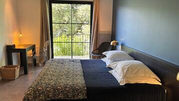 Ein Schlafzimmer mit einem Bett, einem Sessel, einem Tisch und Blick ins Grüne durch ein Fenster.