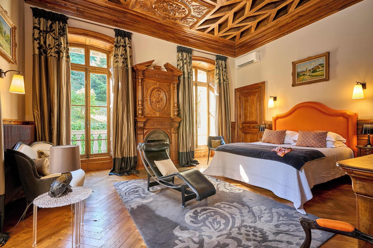 A room with a bed, a chair, a table, and a fireplace.