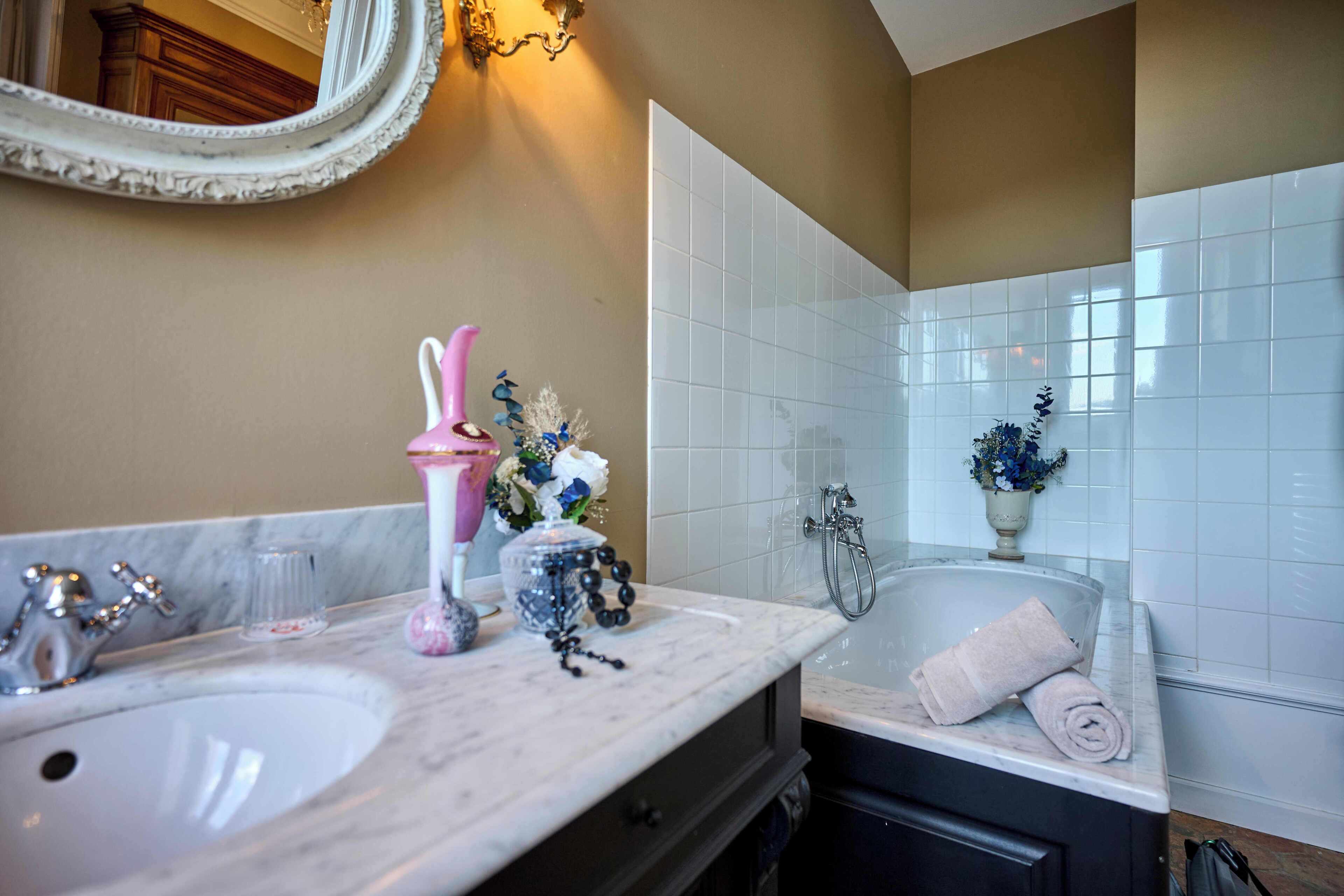 A bathroom with two sinks, a bathtub, a mirror, and a vase with flowers.