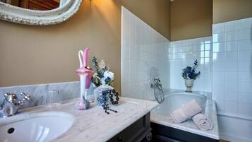 A bathroom with two sinks, a bathtub, a mirror, and a vase with flowers.