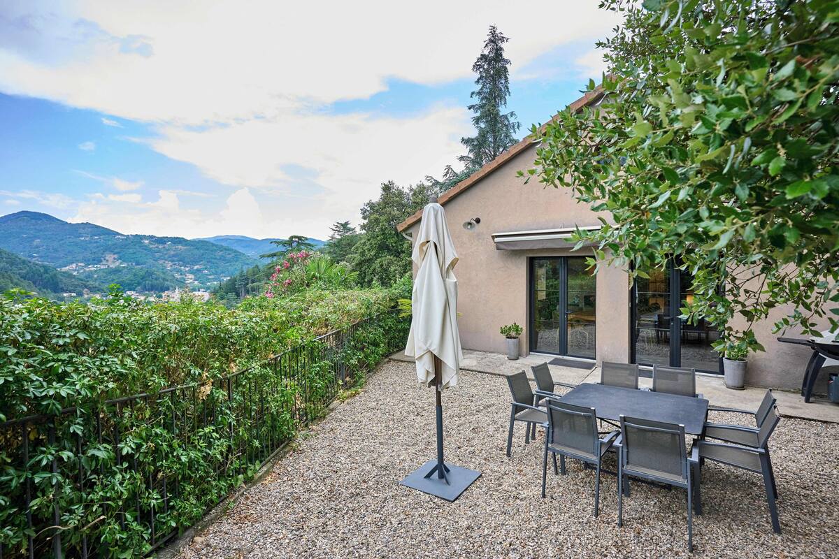 A patio with a table and chairs, a covered umbrella, and a view of hills and mountains.