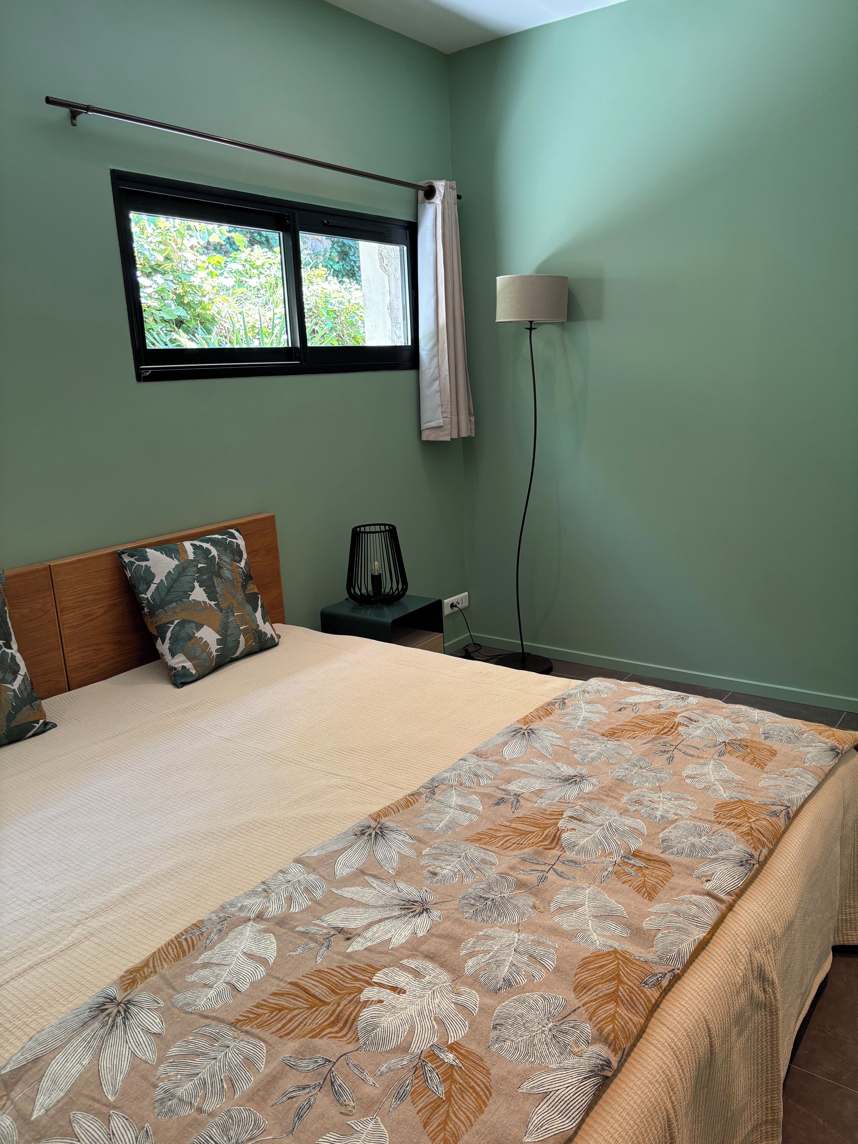 A bedroom with a bed, a nightstand, a lamp, and a window with curtains.