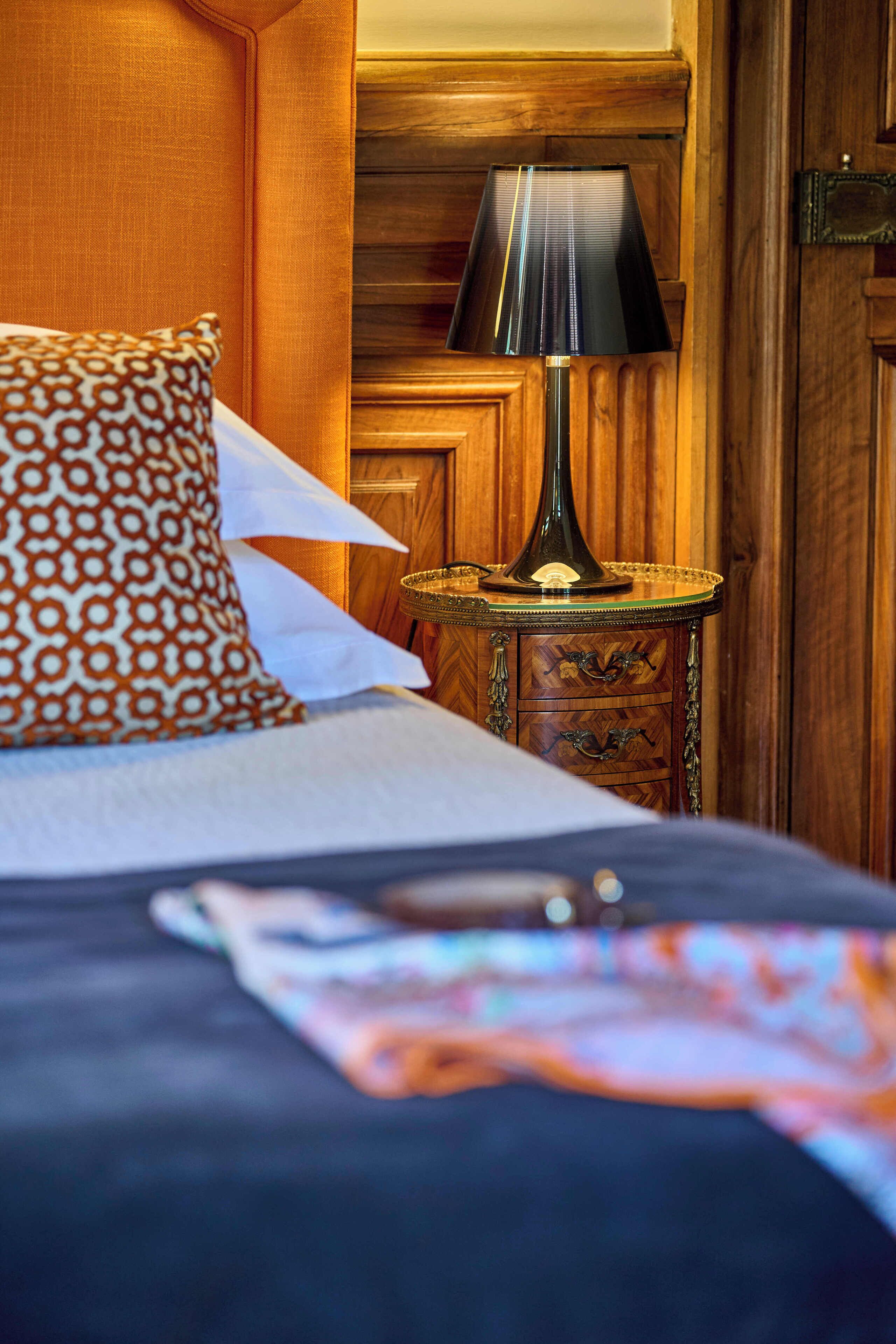 A bed with patterned pillows, a bedside table with a lamp, and wooden paneling.