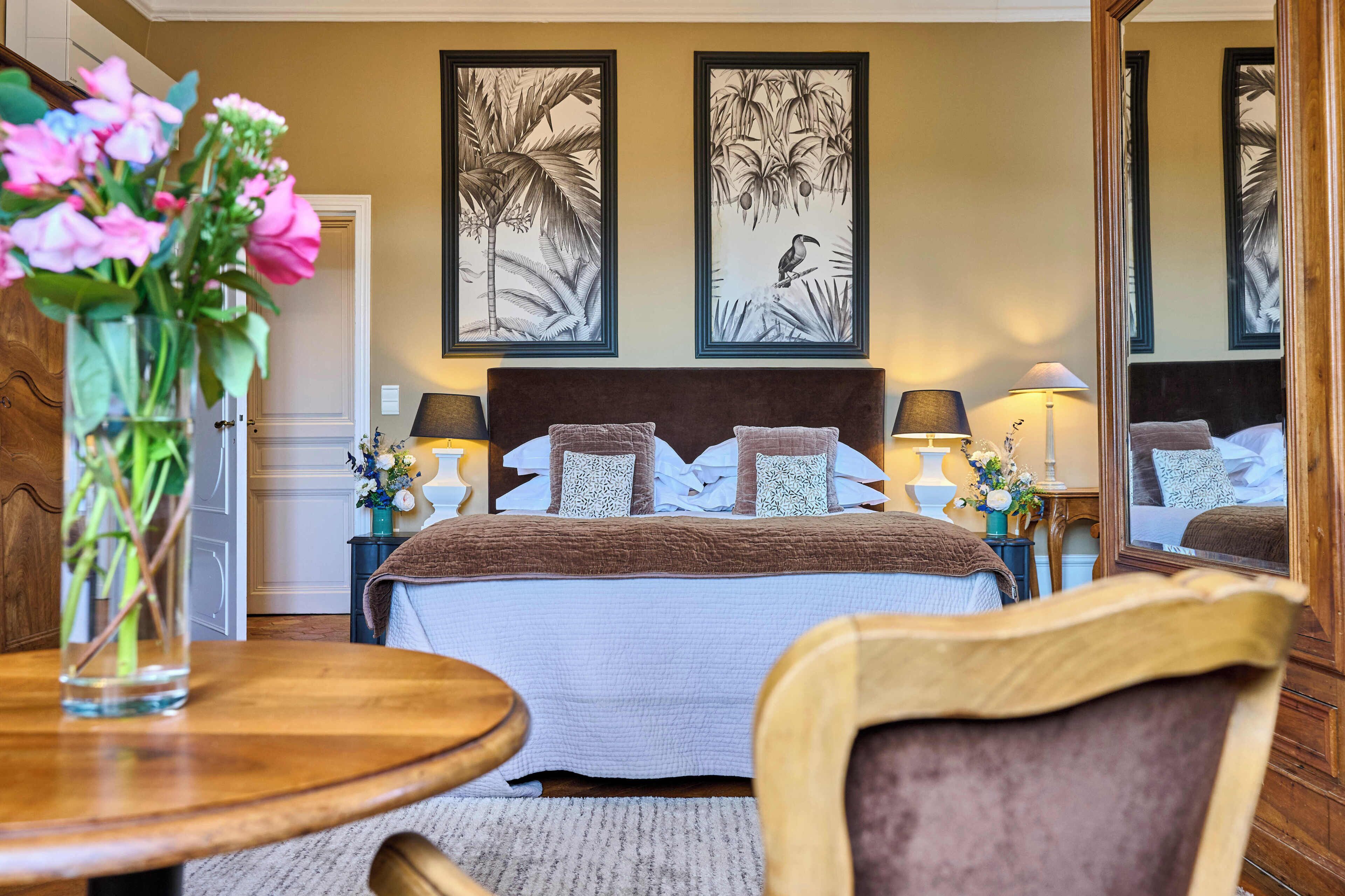 A hotel room with a bed, nightstands, a mirror, and a vase of flowers.