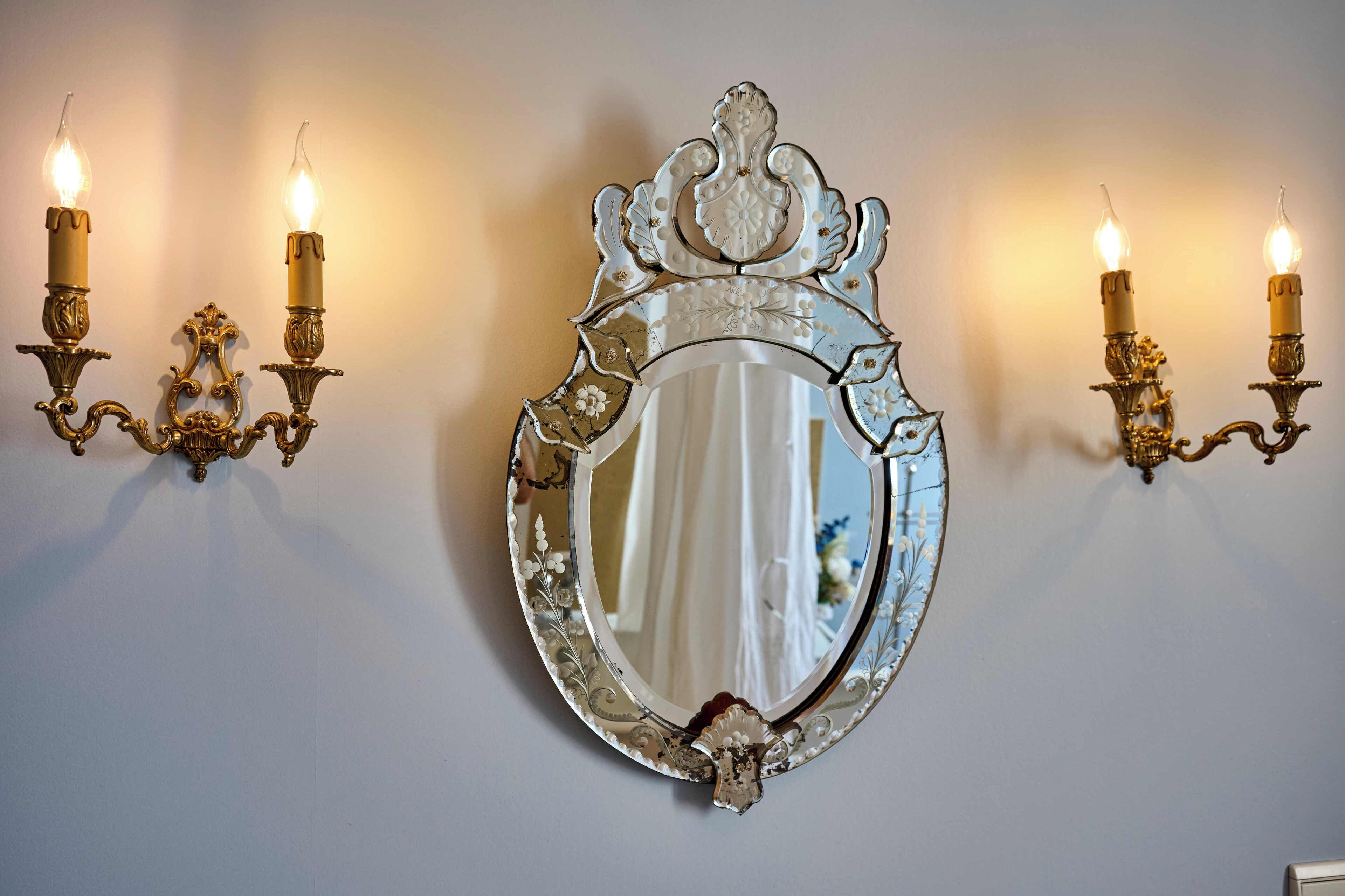 A wall-mounted mirror with ornate gold and white candle sconces on either side.
