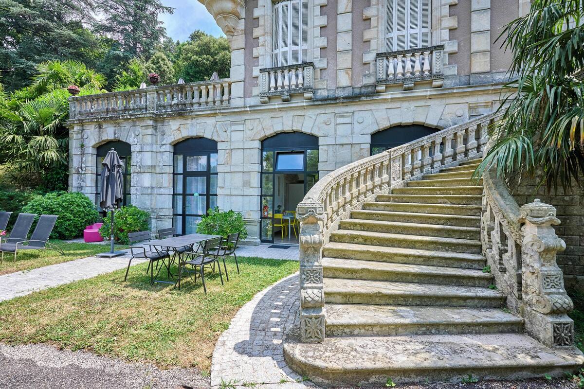 A stone building with a grand staircase, outdoor seating, and lush greenery.