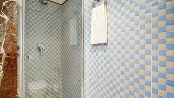 A bathroom with checkered blue and beige tiles, a white towel hanging on a rack, and a shower with a glass door.