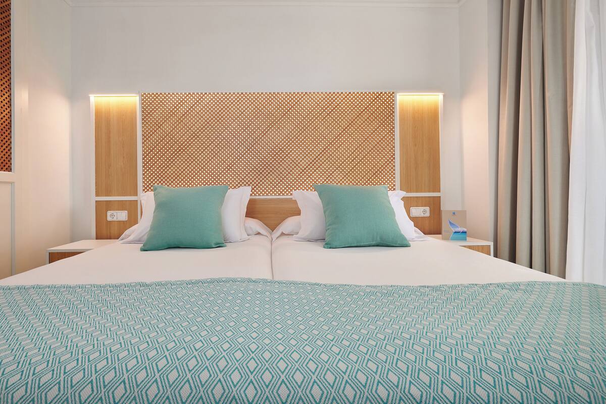 Habitación de hotel con una cama grande, dos almohadas, cabecera de madera y un panel de pared con diseño.