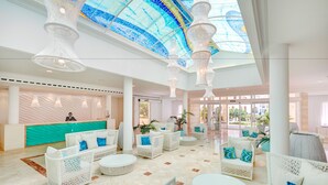 A spacious lobby with white wicker furniture, a reception desk, and a large glass ceiling. - Grupotel Club Turquesa Mar (Ciutadella de Menorca)