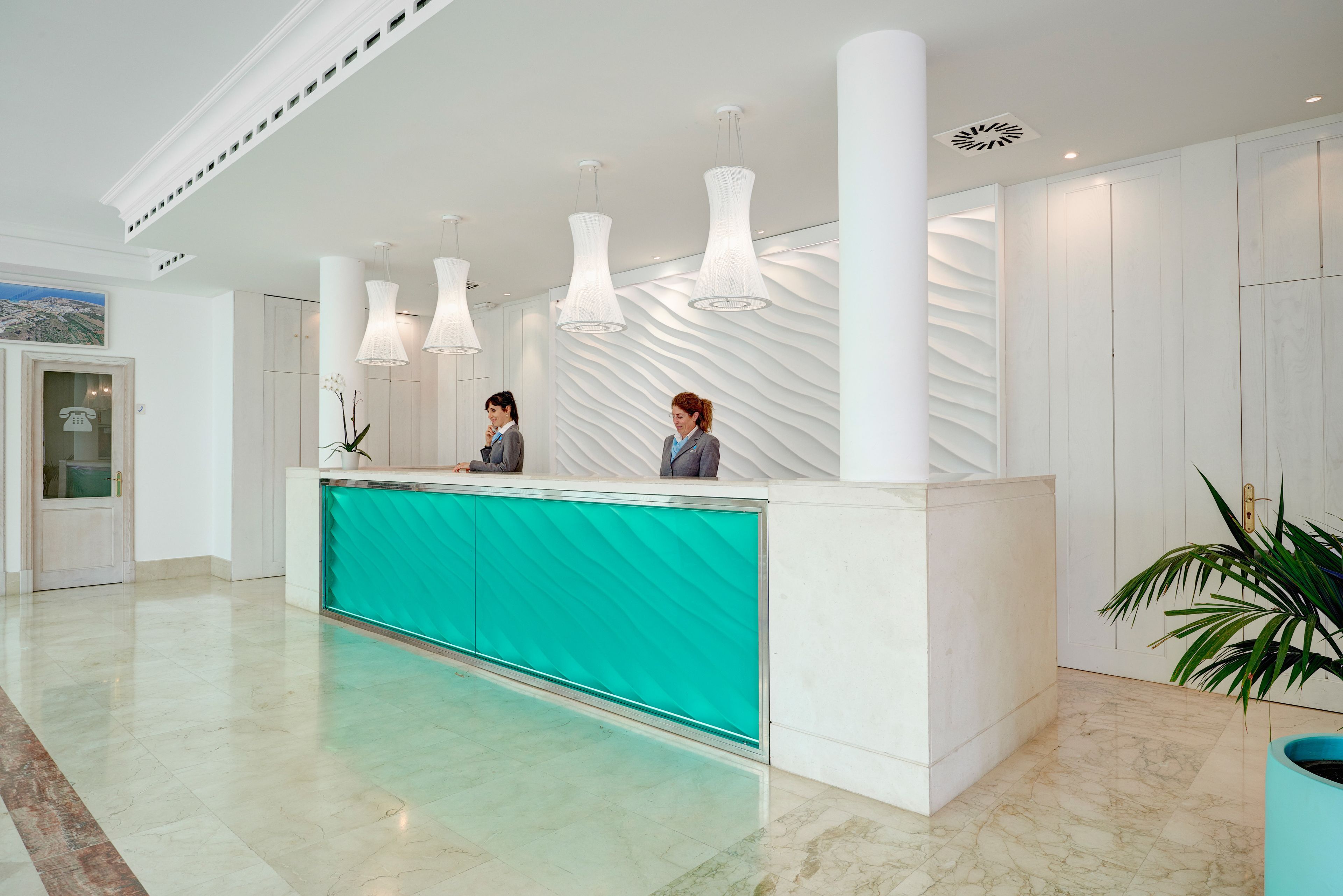 A reception area with a teal counter, white walls, and modern pendant lighting.