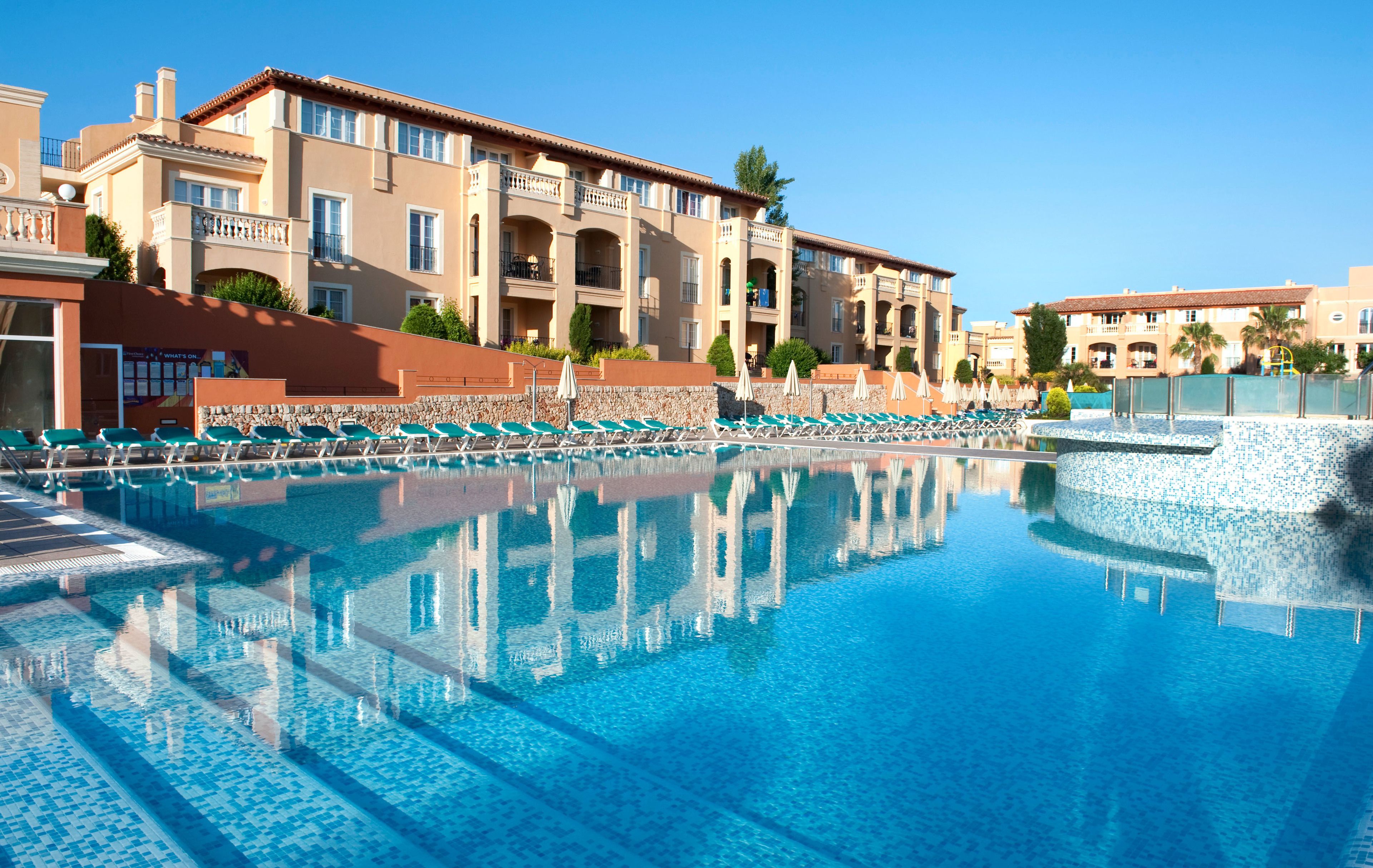 Ein Hotel mit Swimmingpool, mehreren Balkonen und blauem Himmel.