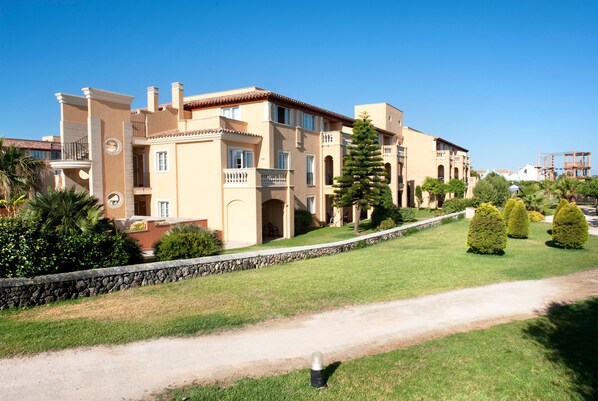 Un hotel de varios pisos con fachada de piedra, balcones y un césped bien cuidado.