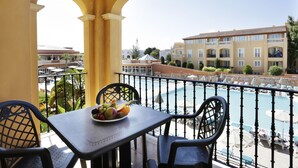 A balcony with a table set for two, overlooking a swimming pool and a building with balconies. - Grupotel Club Turquesa Mar (Ciutadella de Menorca)