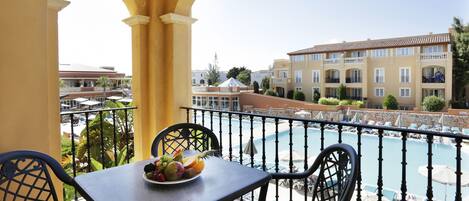 Un balcón con una mesa para dos, con vista a una piscina y un edificio con balcones.