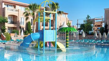 Un área de piscina con tobogán de agua, sillas de descanso y una palmera.