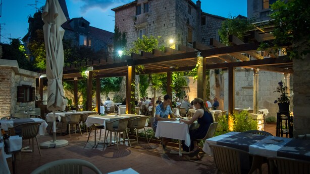 An outdoor dining area with tables and chairs, surrounded by stone buildings and greenery. - Villa Sv. Petar (Trogir)