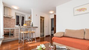 A modern living room with a sofa and a coffee table, a kitchen with a stove and chairs, and a framed picture on the wall. - Villa Sv. Petar (Trogir)