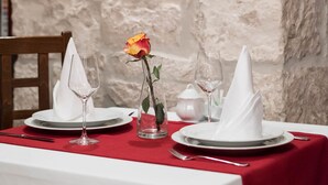 A dining table set with white plates, napkins, and wine glasses, against a white stone wall with a framed picture above. - Villa Sv. Petar (Trogir)