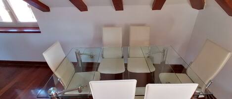 Une salle de conférence dotée d’une table en verre et de chaises blanches, de poutres en bois au plafond et d’une fenêtre laissant entrer la lumière naturelle.