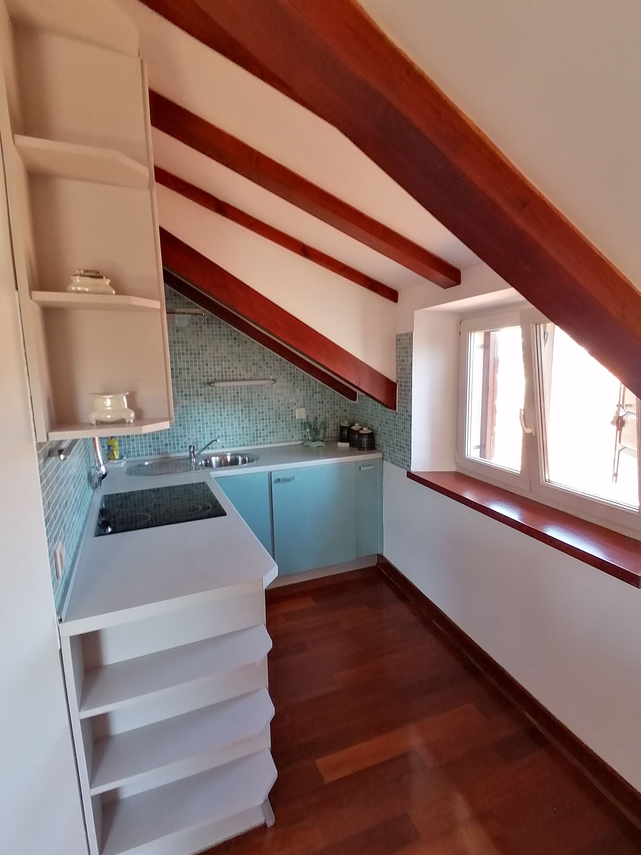 A kitchen with a tiled backsplash, a sink, and wooden beams.