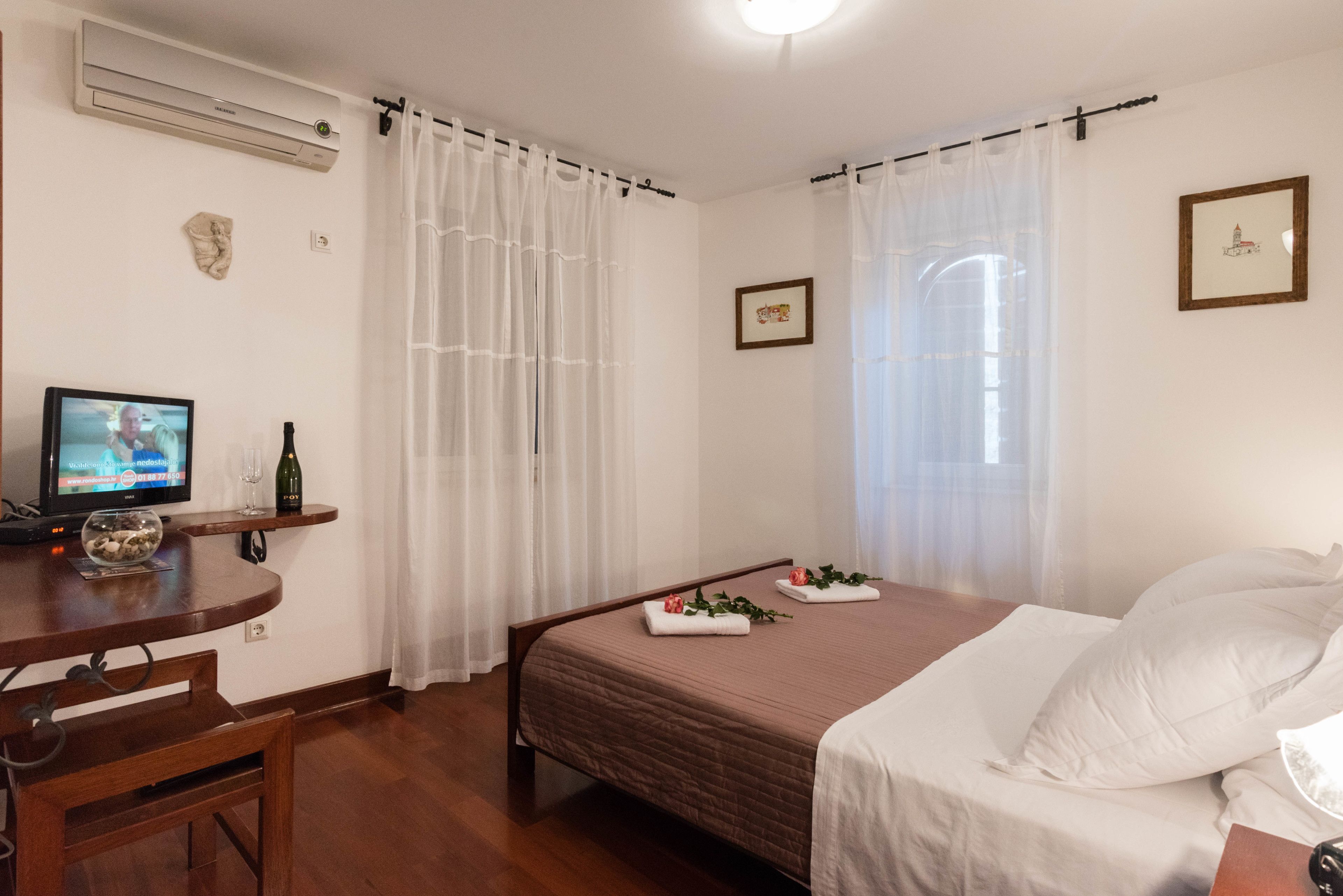 A bedroom with a bed, a desk with a computer, a bottle of wine, and a small decorative item.