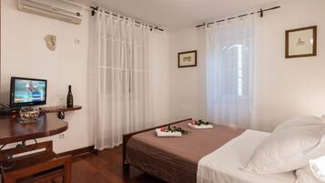 A bedroom with a bed, a desk with a computer, a bottle of wine, and a small decorative item.