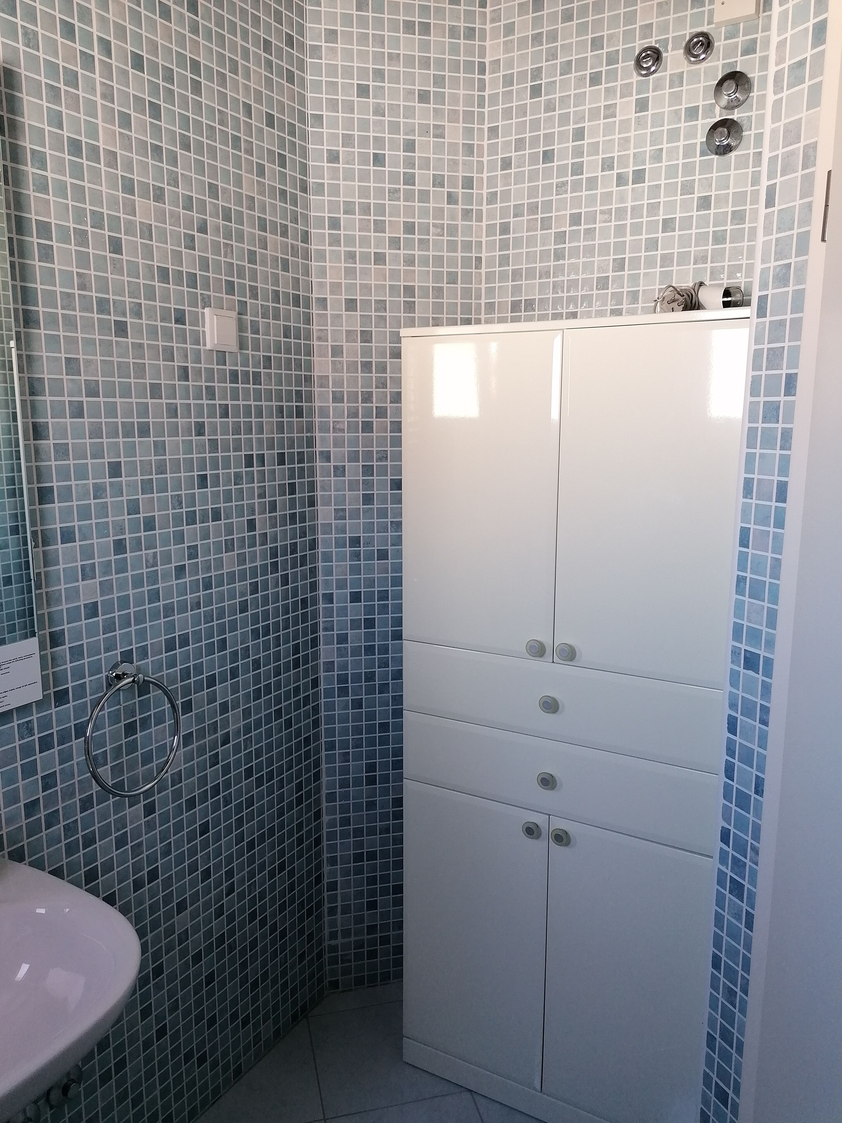 Un baño con paredes de azulejos azules, un mueble blanco con cajones y un lavamanos.