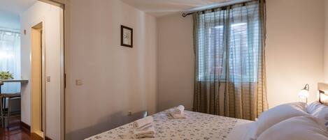 A hotel room with a bed, a desk, and a window with curtains.