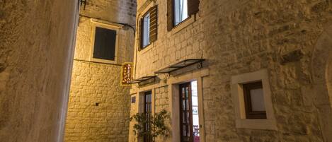 A narrow alleyway with stone buildings, a potted plant, and a sign.