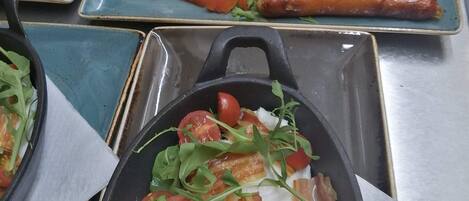 Un bufé con diversos platos, entre ellos huevos revueltos, tocino, salchichas y ensaladas.
