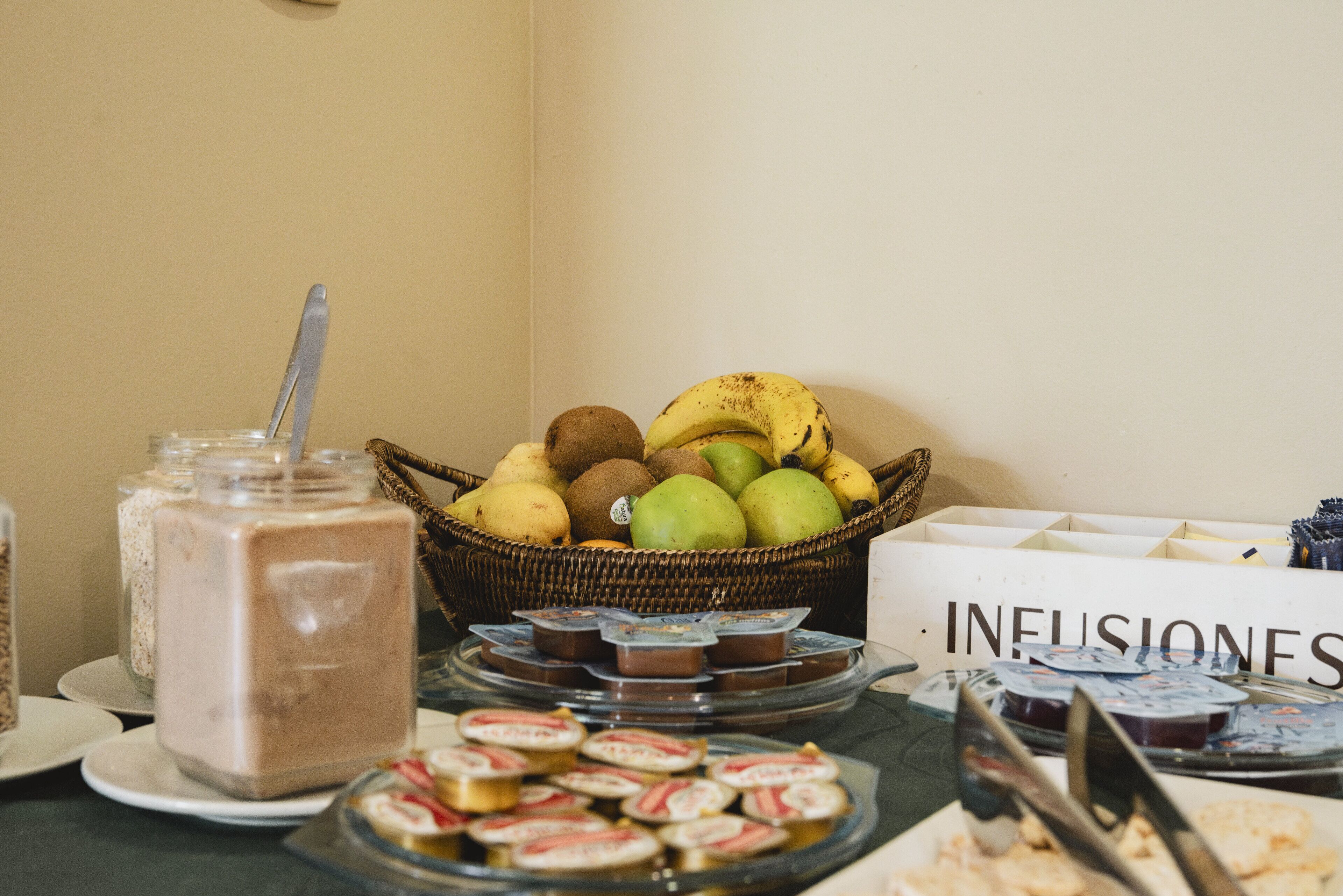 A buffet table with various food items including a basket of fruits, a jar of chocolate mousse, and several trays of desserts.