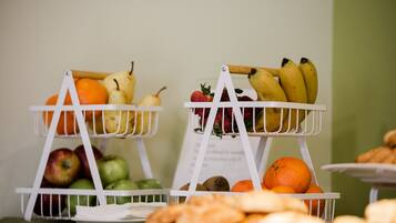 Dos cestas blancas de fruta sobre una mesa con diversas frutas y pasteles.