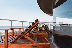 Outdoor wooden lounge chairs and tables on a terrace with a view of the ocean. - Punta Trouville Hotel (Montevideo)