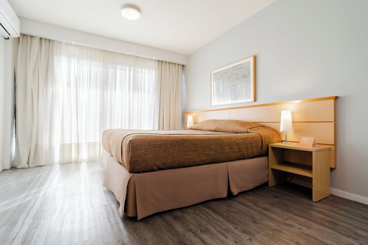 Un cuarto de hotel con una cama grande, una mesita de noche con lámpara y un cuadro enmarcado en la pared.