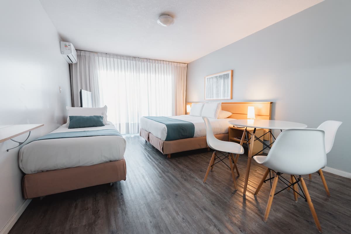 Habitación de hotel con dos camas, un escritorio, una silla, una mesa y una lámpara.