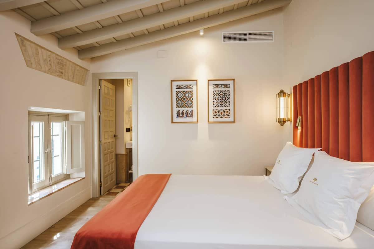 A bedroom with a bed, a window, a door, and two framed wall decorations.