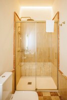 Ducha a ras de suelo con puerta de cristal, una toalla blanca colgada en la puerta y suelo de baldosas.