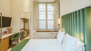 Een hotelkamer met een bed, een bureau met stoel, een spiegel en een raam met uitzicht.