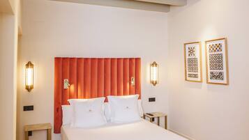 Une chambre d’hôtel avec un grand lit, une tête de lit rouge, deux lampes fixées au mur et un plafond orné de carreaux décoratifs.