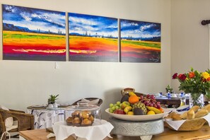 A dining table with a fruit bowl, bread basket, and a vase of flowers.