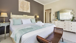 Quarto de hotel bem arrumado com uma cama grande, duas mesas de cabeceira com luminárias, um banco de madeira, uma cômoda e um espelho.